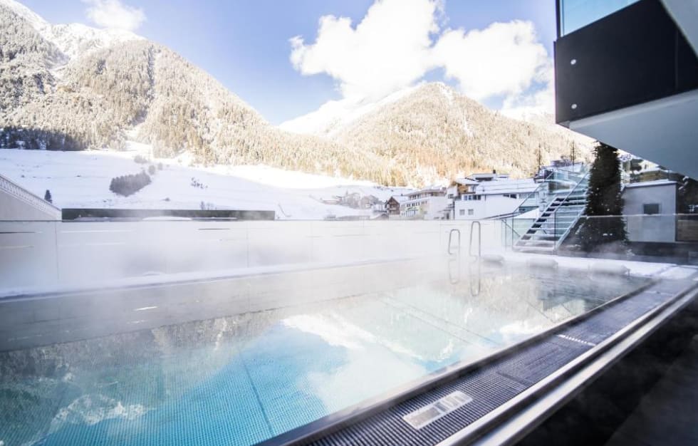 Dampfender Außenpool eines Wellnesshotels in Ischgl mit Blick auf schneebedeckte Berge – passend zu Skipasspreise Österreich und Ischgl Skipass.